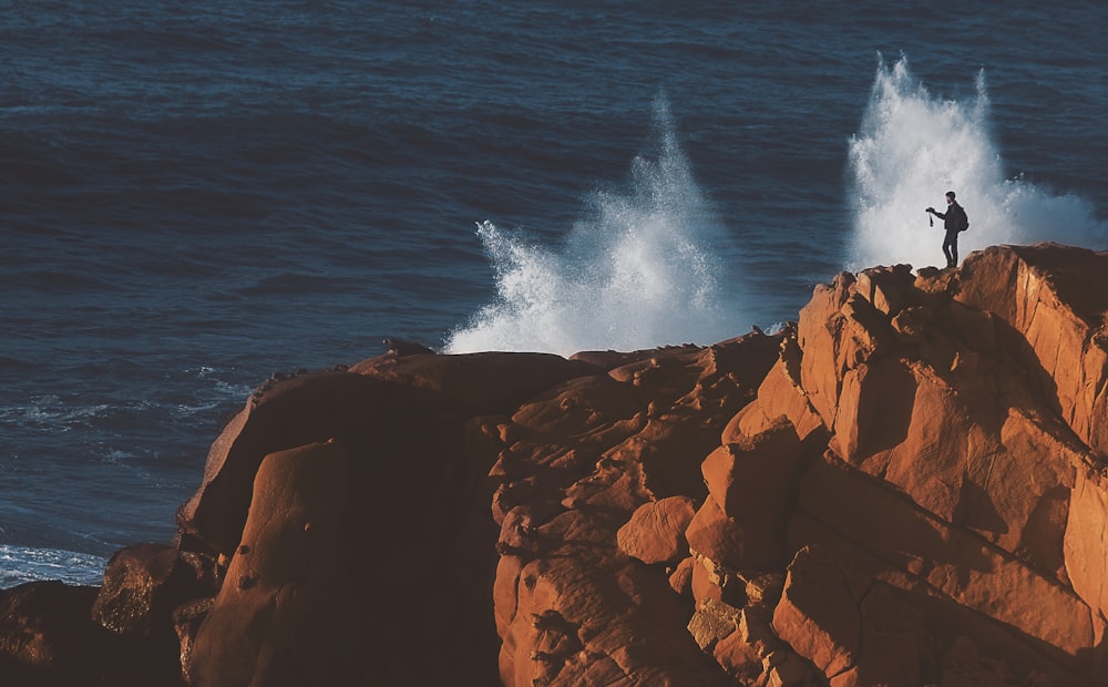 man standing on brown cliff near body of water during daytime