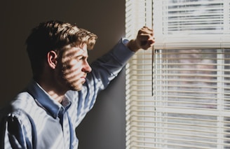 man near clear glass window pane and window blinds craving a relationship that stretches his limits