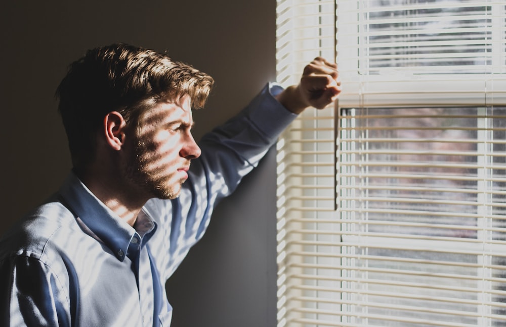 personne à proximité d’une vitre en verre transparent et de stores de fenêtre photographie en basse lumière