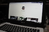 A laptop displaying a social media profile page with various elements such as a profile picture, username, and links. Below the main header, there are sections for photos and collections, showing preview images. The laptop keyboard is visible in the lower part of the image.