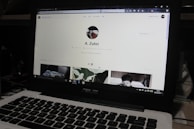 A laptop displaying a social media profile page with various elements such as a profile picture, username, and links. Below the main header, there are sections for photos and collections, showing preview images. The laptop keyboard is visible in the lower part of the image.