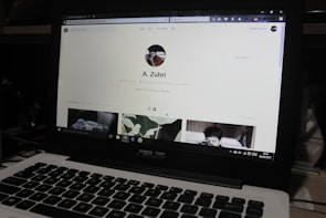 A laptop displaying a social media profile page with various elements such as a profile picture, username, and links. Below the main header, there are sections for photos and collections, showing preview images. The laptop keyboard is visible in the lower part of the image.