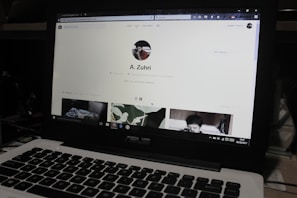 A laptop displaying a social media profile page with various elements such as a profile picture, username, and links. Below the main header, there are sections for photos and collections, showing preview images. The laptop keyboard is visible in the lower part of the image.