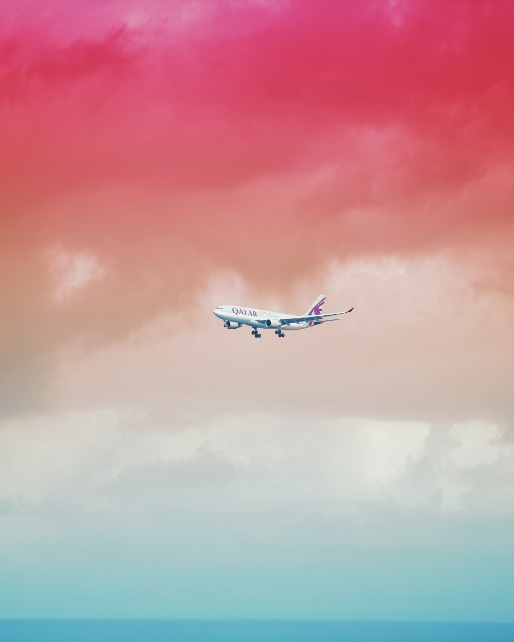 Flugzeug der Qatar Airlines fliegt unter roter Wolkenformation