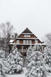 A warm-toned prefabricated cottage nestled on a snowy hillside under an overcast sky.