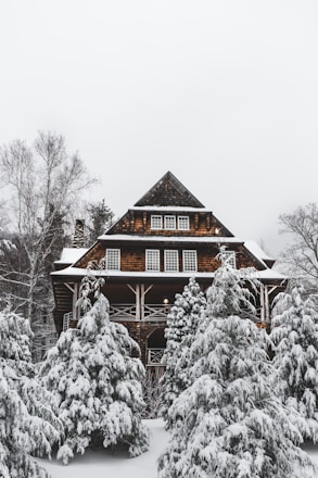 A warm-toned prefabricated cottage nestled on a snowy hillside under an overcast sky.