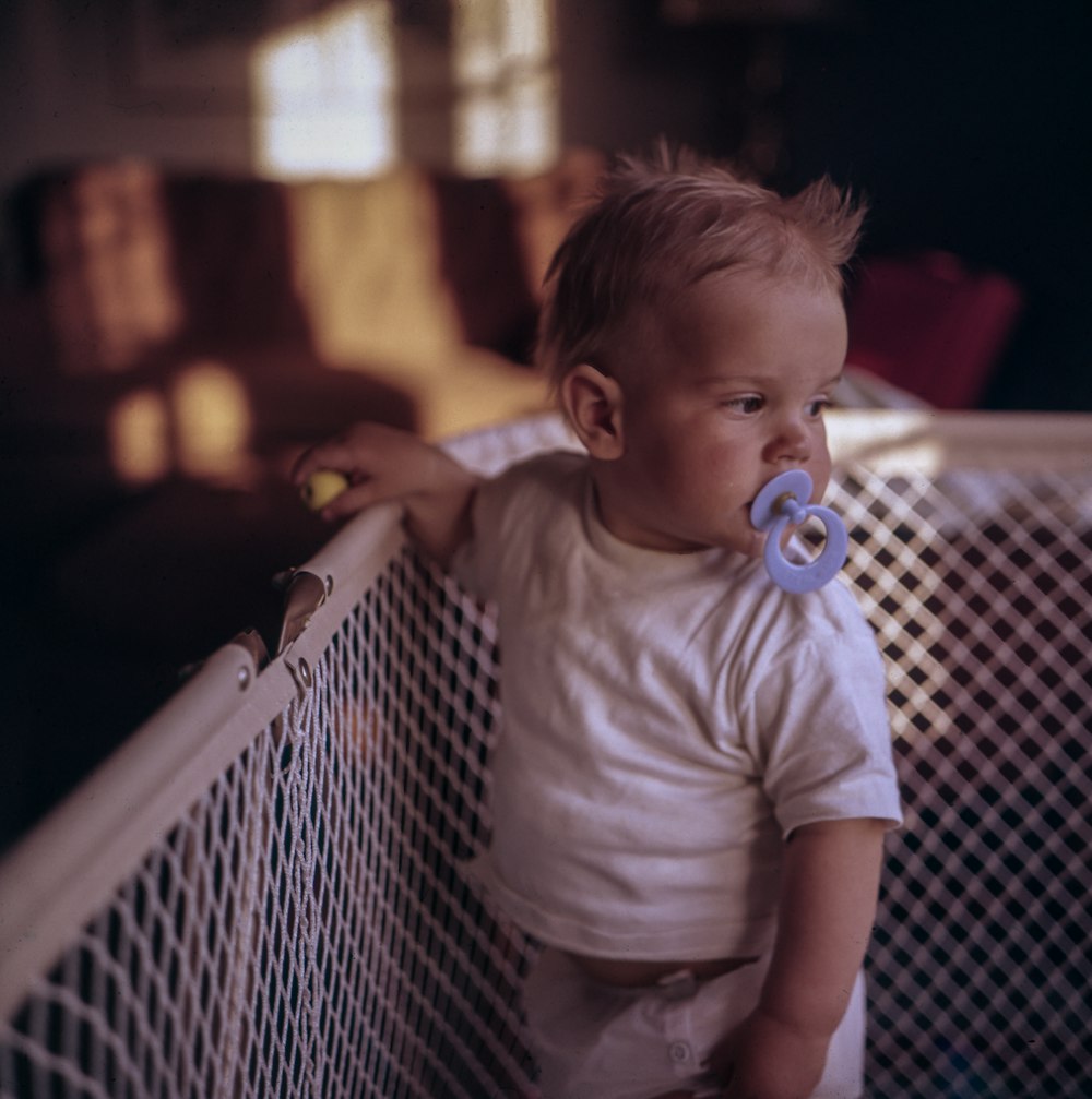 Baby mit lila Schnuller steht auf Kinderbett