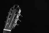 A close-up view of the headstock of a classical guitar, showcasing its tuning pegs, strings, and intricate design details against a dark background.