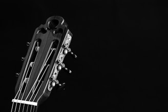 A close-up view of the headstock of a classical guitar, showcasing its tuning pegs, strings, and intricate design details against a dark background.