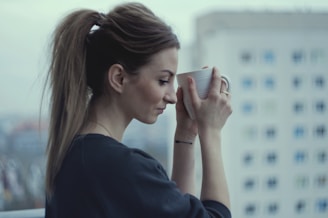 A stylish woman enjoying a serene morning coffee with city views in the background.