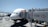 An airplane is parked at an airport gate, connected to a jet bridge marked with the number 150. The HSBC logo is prominently displayed on the jet bridge. Ground service vehicles and equipment are visible on the tarmac, with personnel attending to the aircraft. The sky is clear and blue, indicating good weather conditions.