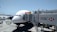 An airplane is parked at an airport gate, connected to a jet bridge marked with the number 150. The HSBC logo is prominently displayed on the jet bridge. Ground service vehicles and equipment are visible on the tarmac, with personnel attending to the aircraft. The sky is clear and blue, indicating good weather conditions.