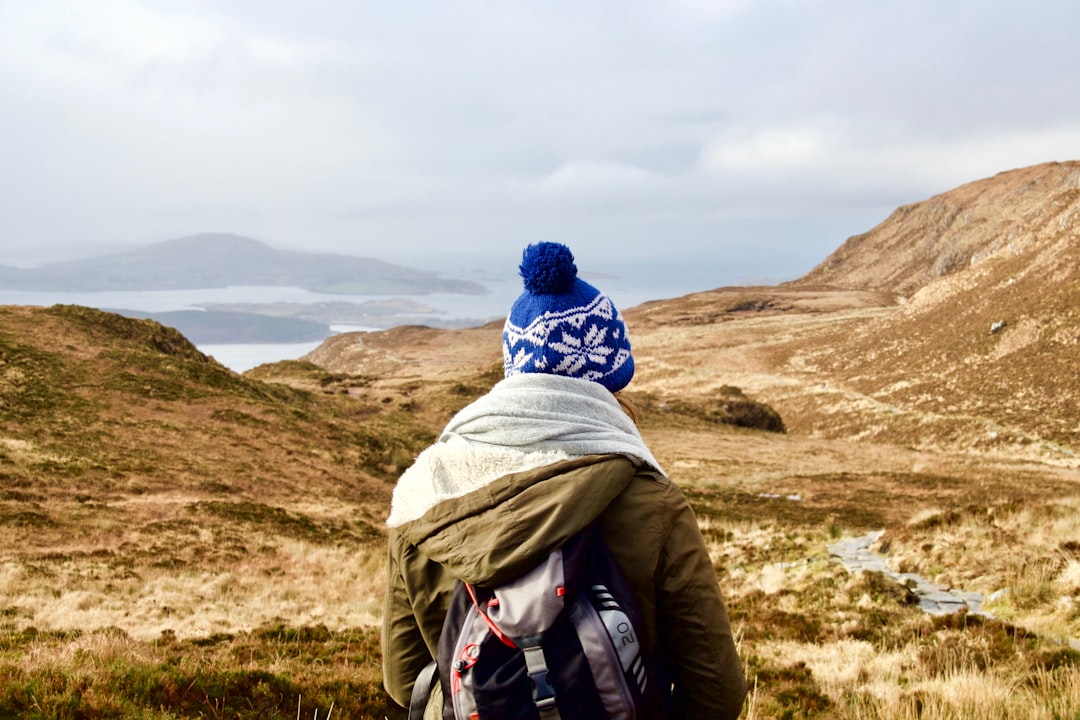 person wearing brown hooded jacket standing on brown mountain during daytime