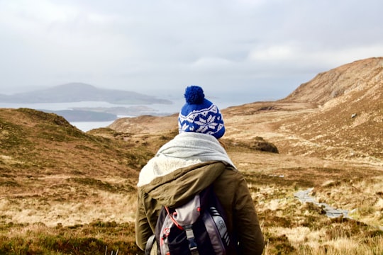 person wearing brown hooded jacket standing on brown mountain during daytime in Diamond Hill Ireland