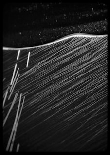 A monochrome image featuring a dynamic play of light and shadows with diagonal lines across the frame. The top section appears textured with a slightly curved, bright edge separating two regions, suggesting abstract movement or flow.
