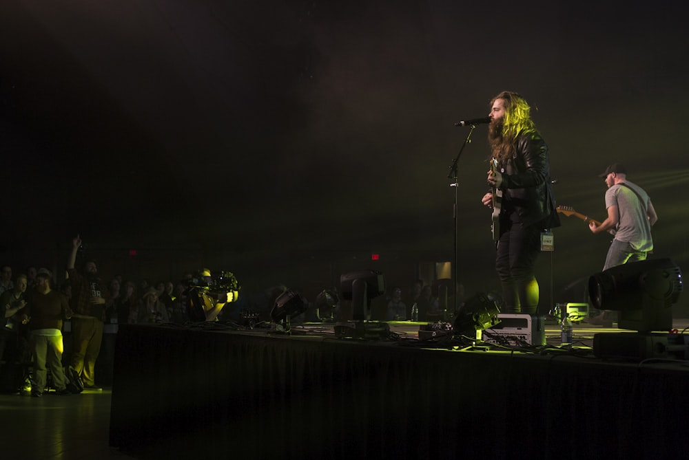 two men playing guitars on stage near people