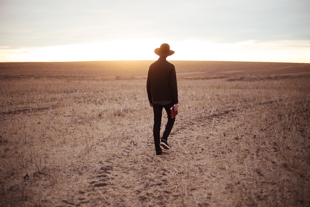 man walking on dried plain while looking towards the sun on horizon