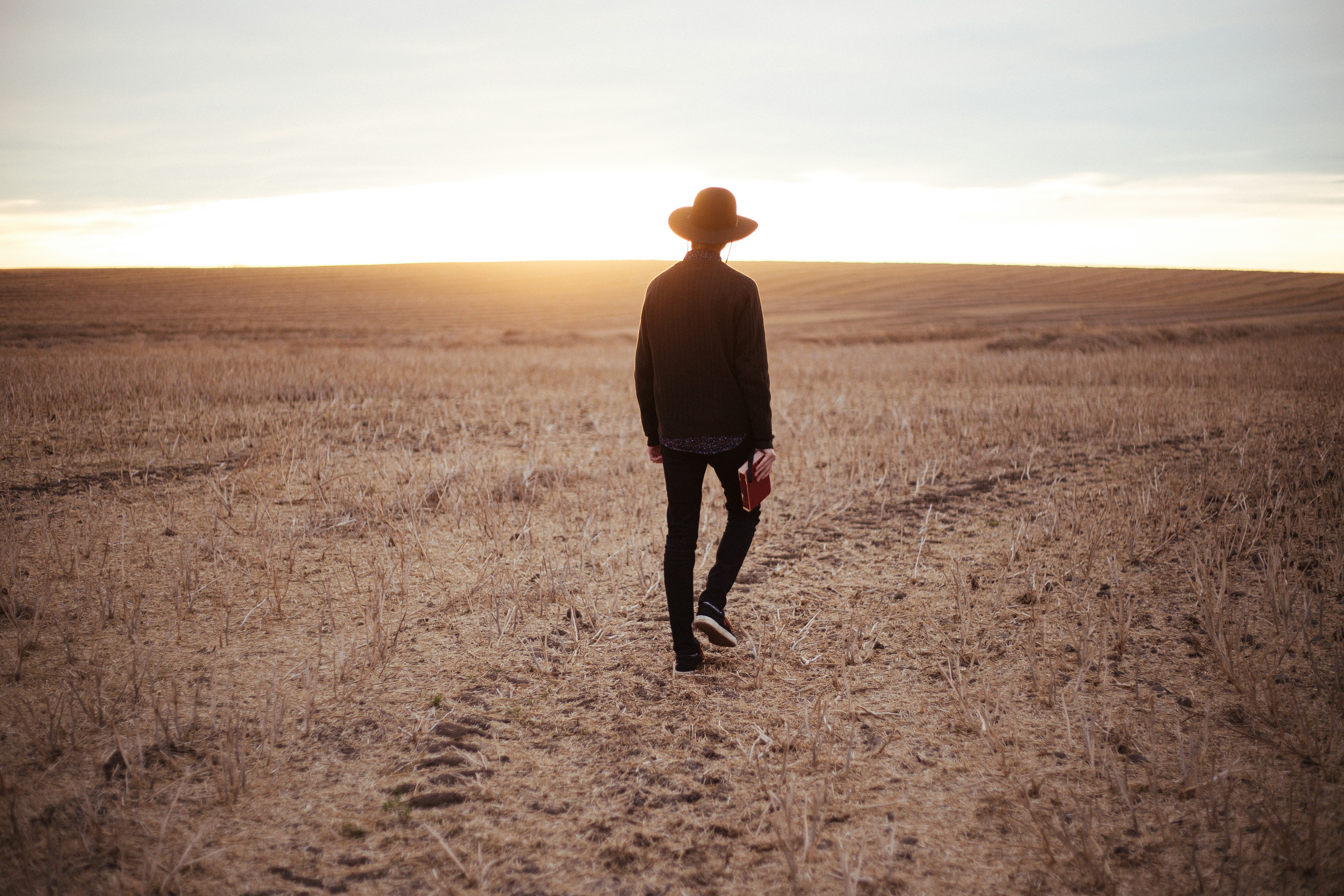 man walking on dried plain while looking towards the sun on horizon