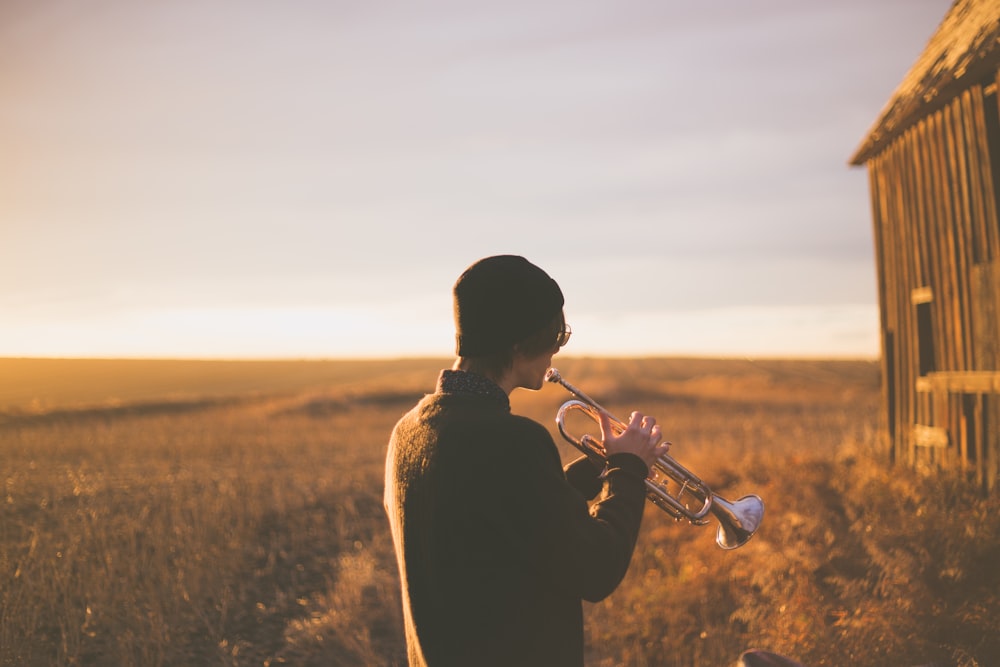man playing trumpet outside house on field during daytime