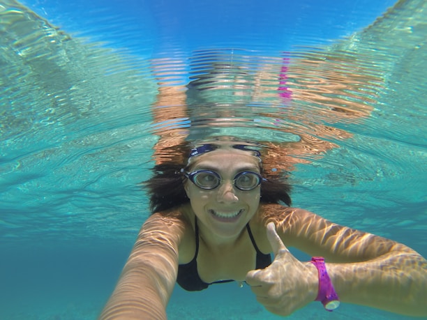 Close-up of a smiling diver giving a thumbs-up underwater with sunlight filtering through the waves above.