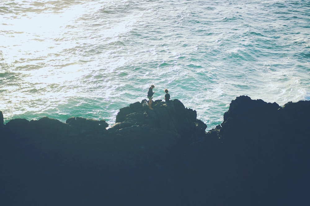 two person standing on the cliff near the ocean