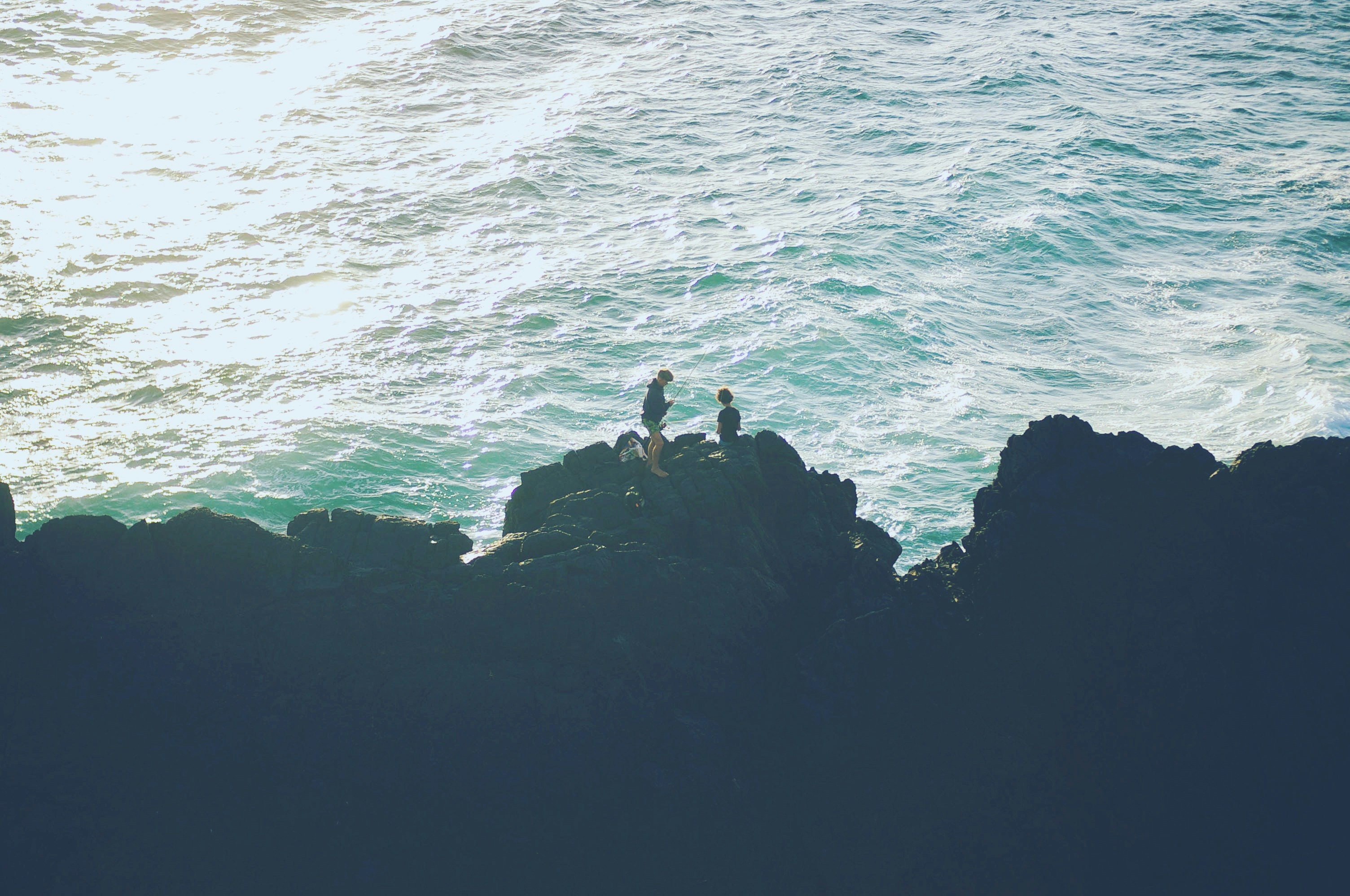 two person standing on the cliff near the ocean
