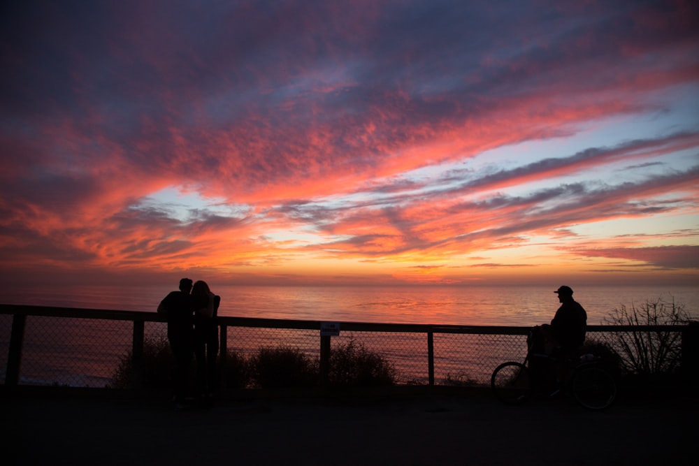 silhouette of people near cliff railings at distance to wide body of water during golden hour