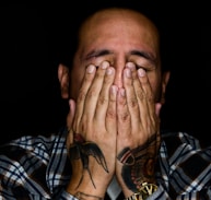 man wearing black, white, and gray plaid sport shirt covering his face