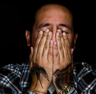 man wearing black, white, and gray plaid sport shirt covering his face