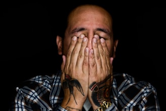 man wearing black, white, and gray plaid sport shirt covering his face