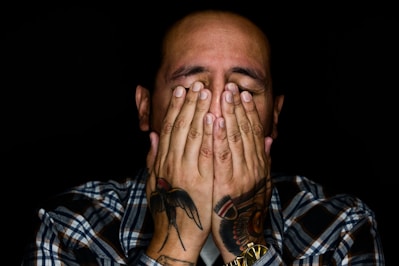 man wearing black, white, and gray plaid sport shirt covering his face