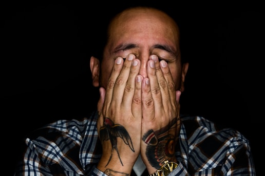 man wearing black, white, and gray plaid sport shirt covering his face