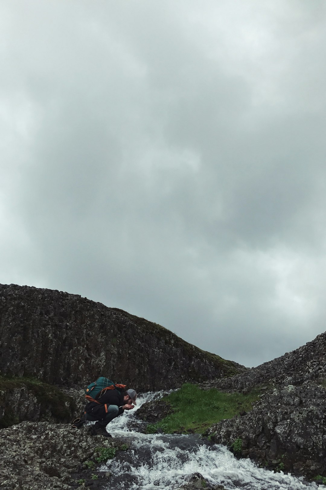 man kneeling near flowing water time lapse photo during cloudy day