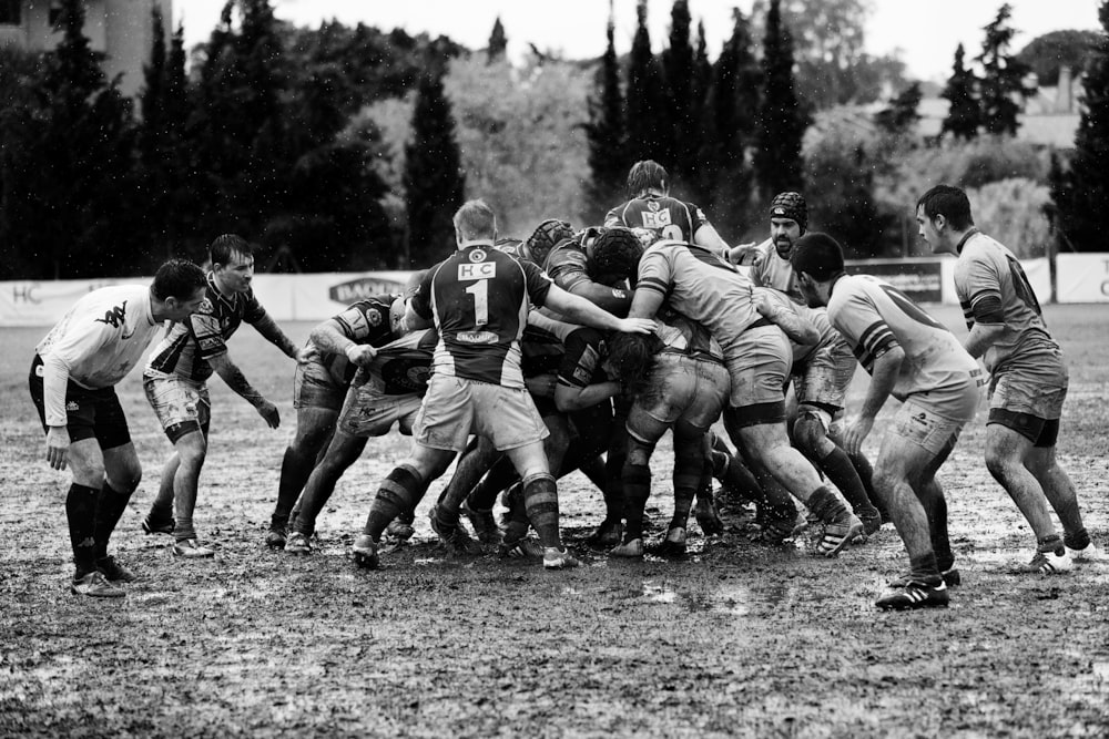 Graustufenfotografie von Männern, die auf schlammigem Land Rugby spielen