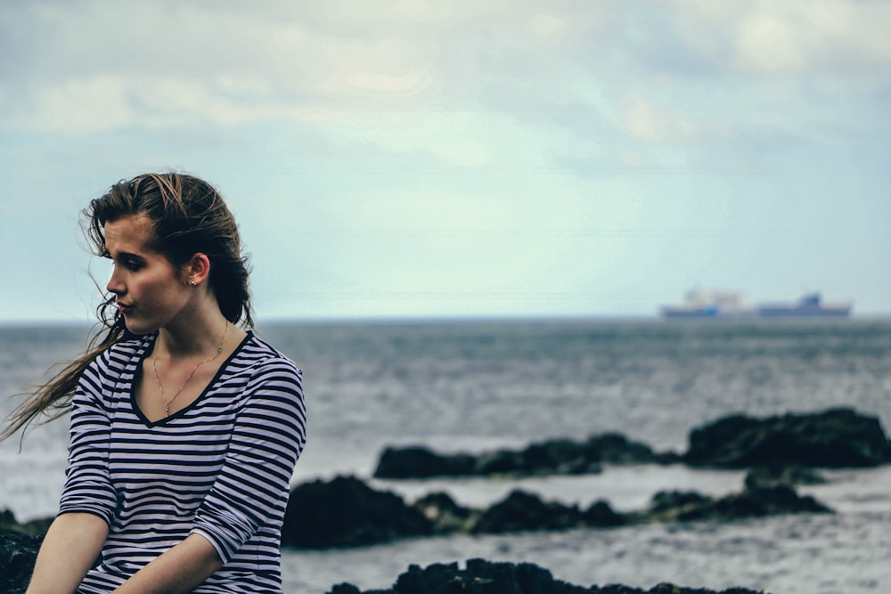 Photographie de mise au point de la femme en noir et blanc rayé col en V chemise à manches coudées près de la mer pendant la journée