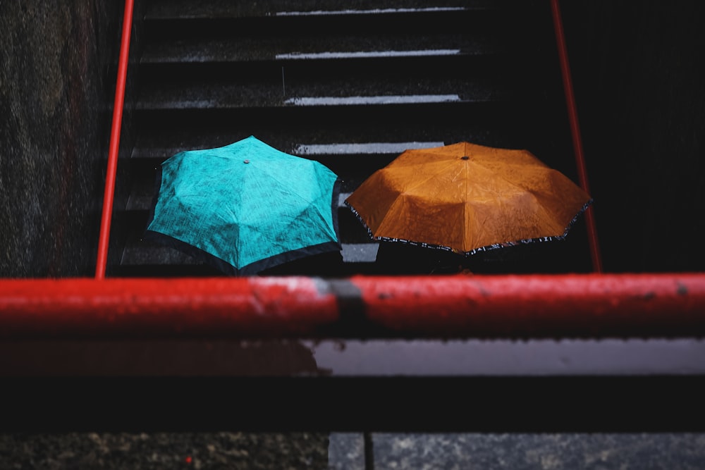 zwei Personen mit blaugrünen und braunen Regenschirmen