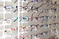 Multiple pairs of eyeglasses arranged neatly on a display rack. The eyeglasses come in various colors and frame styles, and they are evenly spaced and organized in rows.