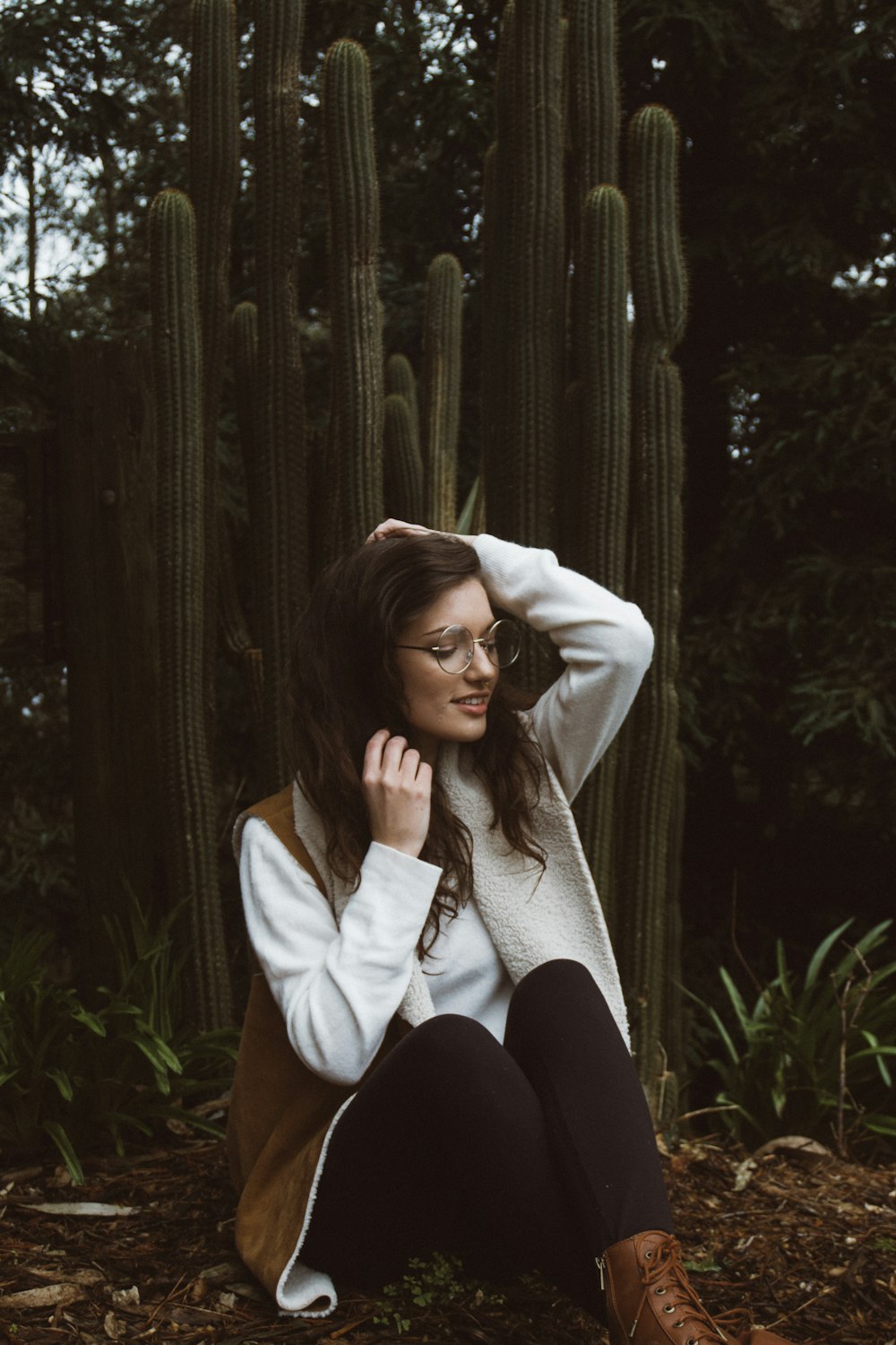 mulher sorridente vestindo casaco marrom e branco sentado ao lado de plantas de cactos verdes