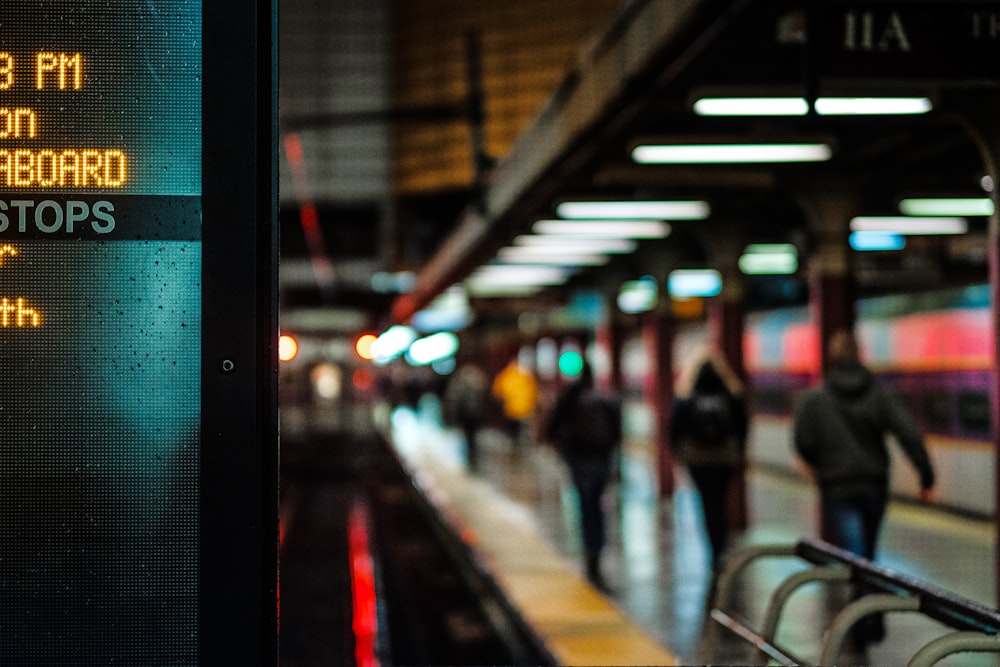 City subway platform lit with signs and commuters walking to their destination