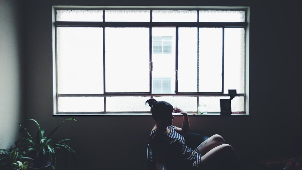 woman sitting on chair beside glass window near plant