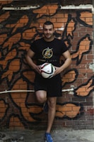 Another young man dressed in a vintage Boca Juniors jersey and retro Adidas pants, leaning casually against a graffiti wall.