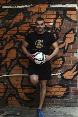 Close-up of a football creator filming himself juggling a ball against a graffiti wall.