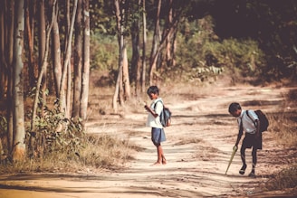 two boys standing on road near tree at daytime