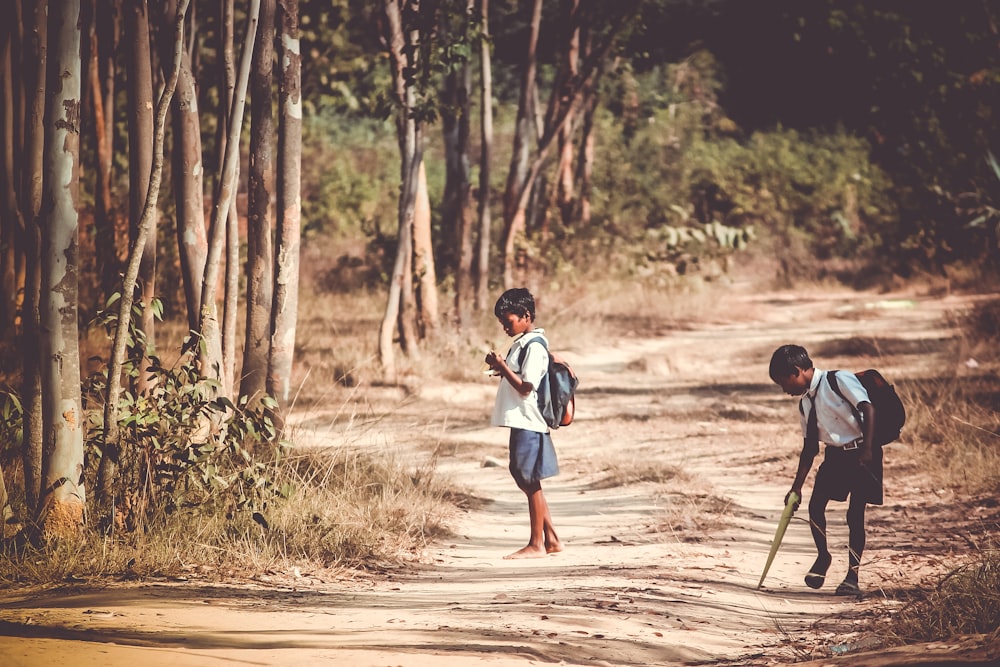 two boys standing on road near tree at daytime