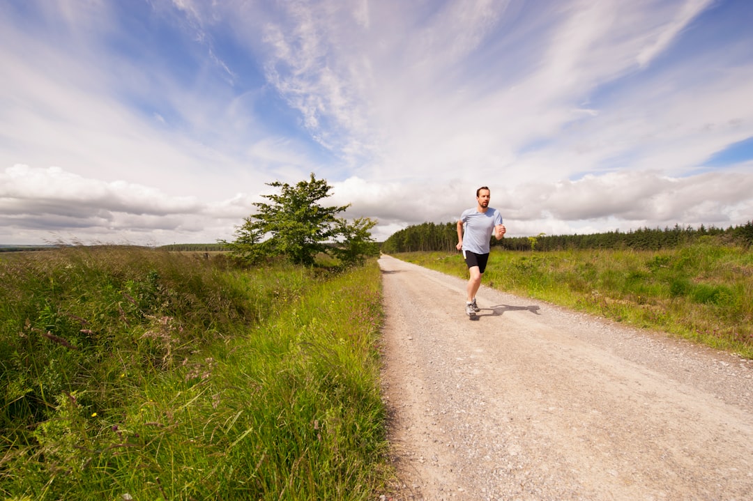 man running on dirt road under cloudy skies