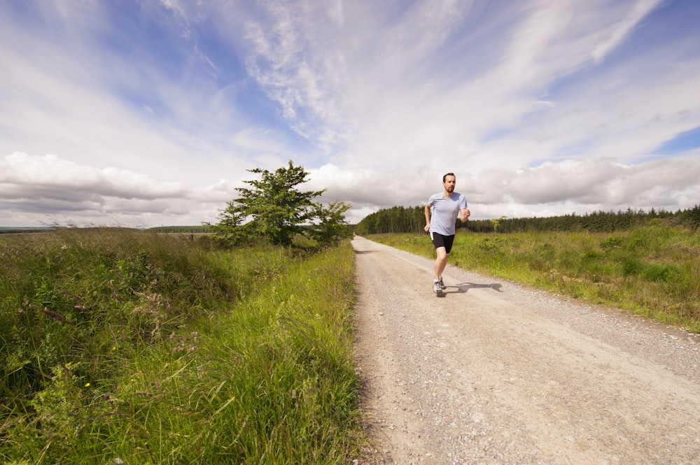 man running on dirt road under cloudy skies