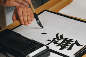 person holding black paint brush while painting black text on white paper