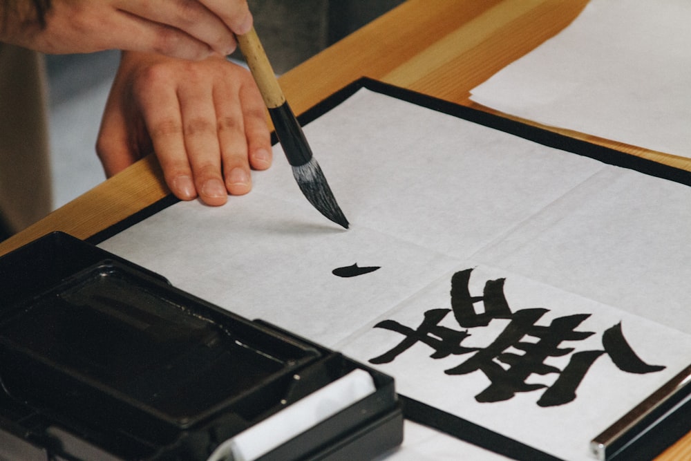pessoa segurando pincel preto enquanto pinta texto preto em papel branco