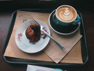 A wooden tray filled with flaky croissants and muffins next to a latte