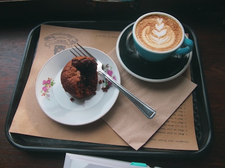 A wooden tray filled with flaky croissants and muffins next to a latte